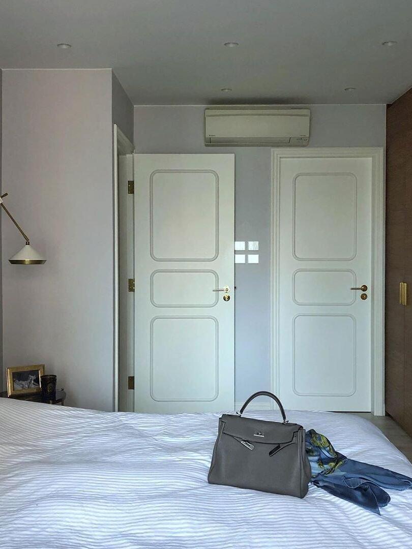 Bedroom scene with white doors, a handbag on the bed and a partial white wall light at the left edge