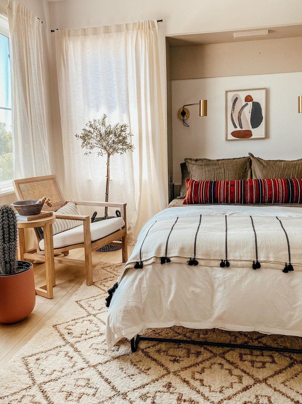Dark cylindrical wall light beside striped bed and framed art
