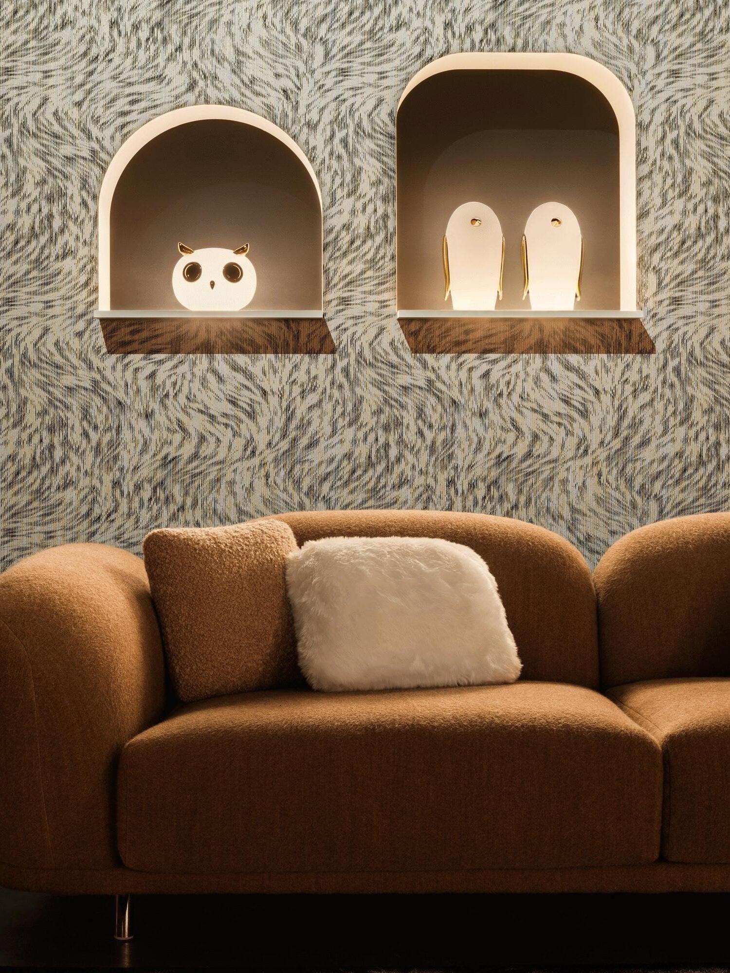 Owl and two penguin lamps in separate arched niches above brown sofa