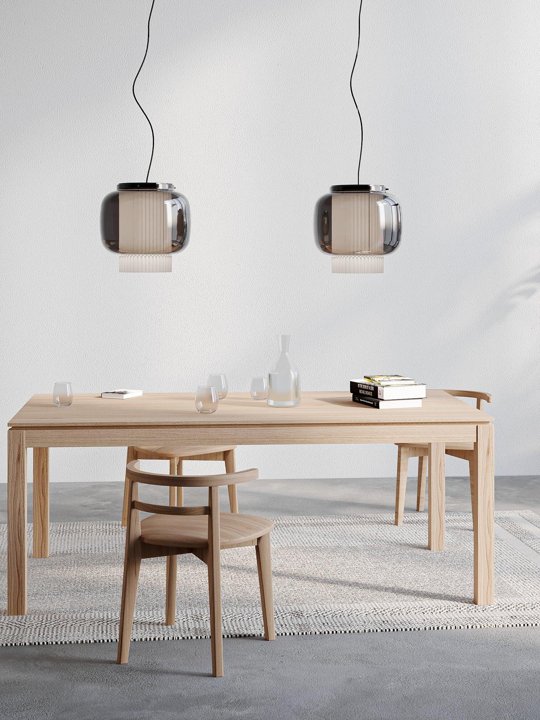 Two smoke-grey Manila T pendant lights above a rectangular wood table with wooden chairs and a water carafe