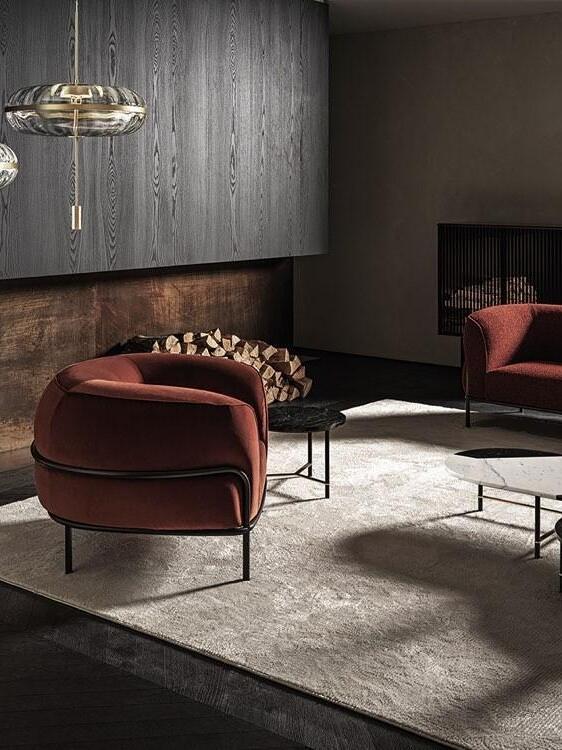 Partly cropped glass pendant above a lounge with rust-coloured armchairs