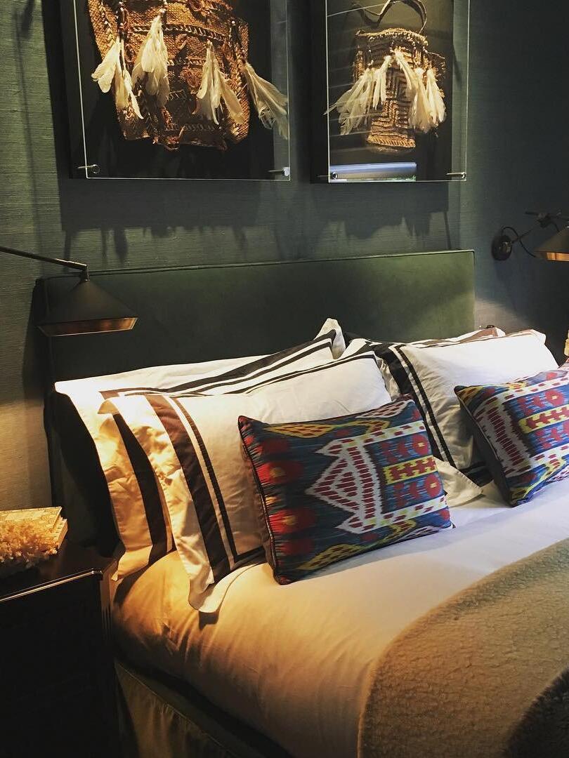 Two black cone wall lights flanking a green headboard with patterned cushions and framed feather art