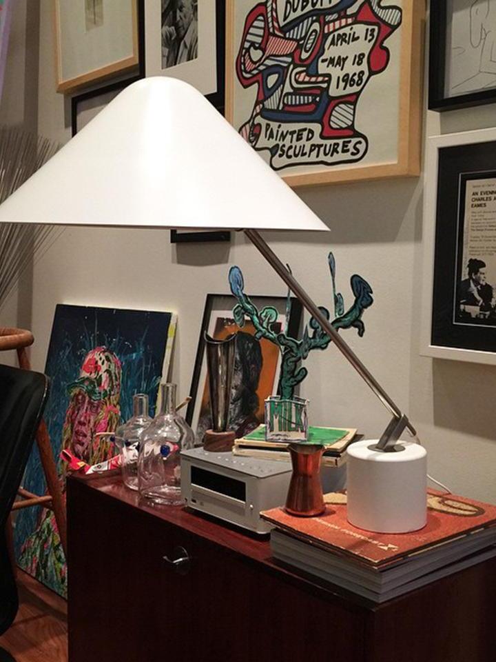 White shade and diagonal arm on a desk among pictures, books and decorative objects