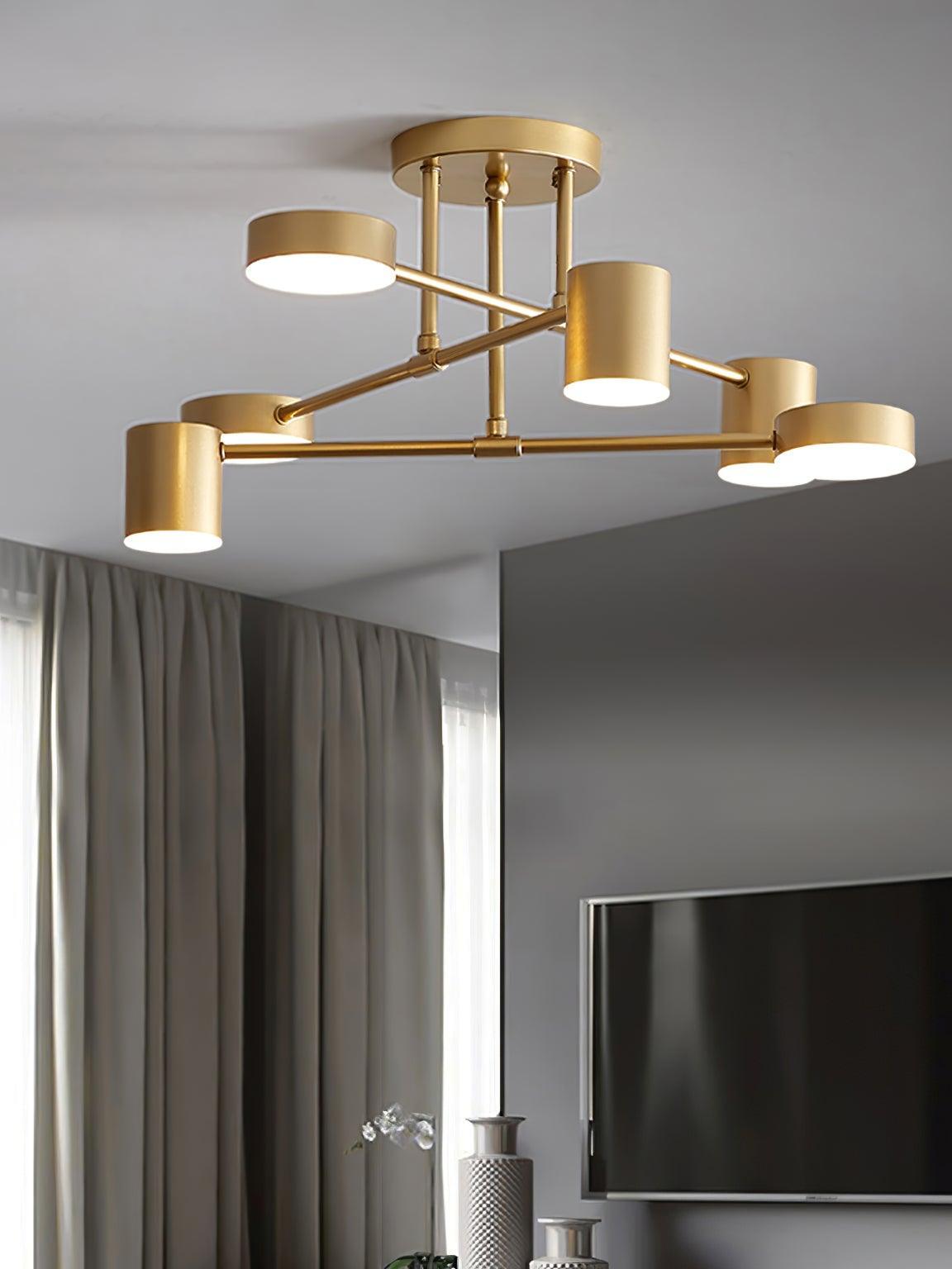 Lit gold crossed-arm ceiling light with six round faces above a gray room with curtains, television and patterned vases