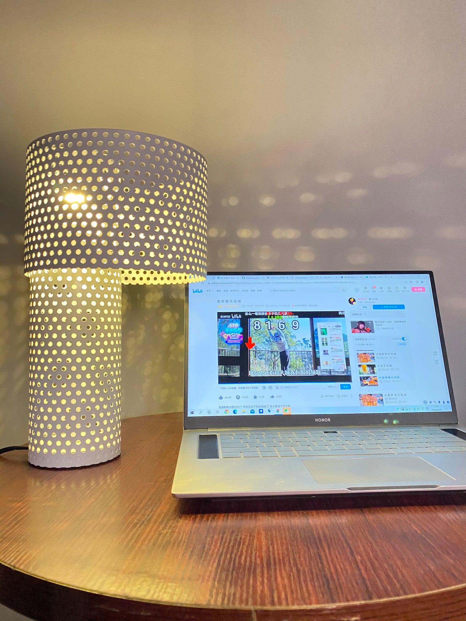 Lit perforated lamp and laptop under dotted wall shadows