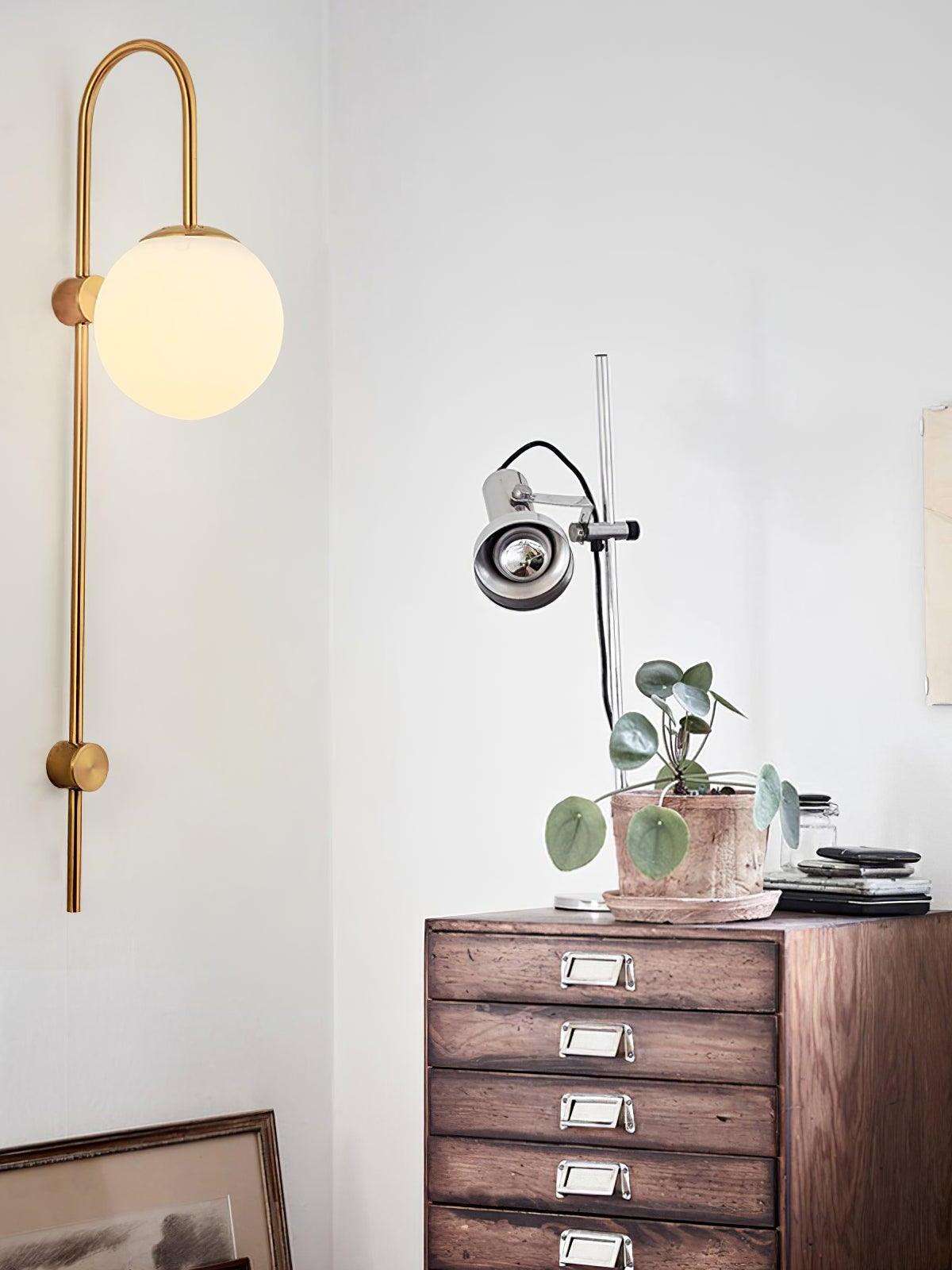 Gold globe wall lamp above a wooden drawer cabinet