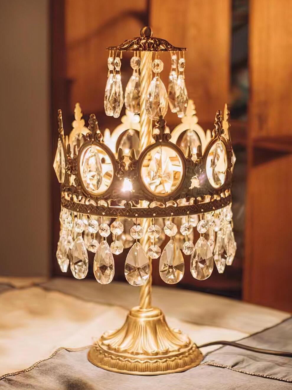 Illuminated crystal table lamp with upper hanging drops on a tabletop in a warm-toned room.