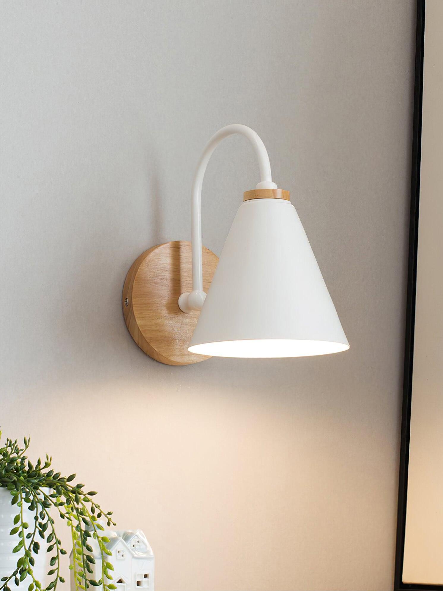 White cone wall lamp glowing beside a plant and wall art