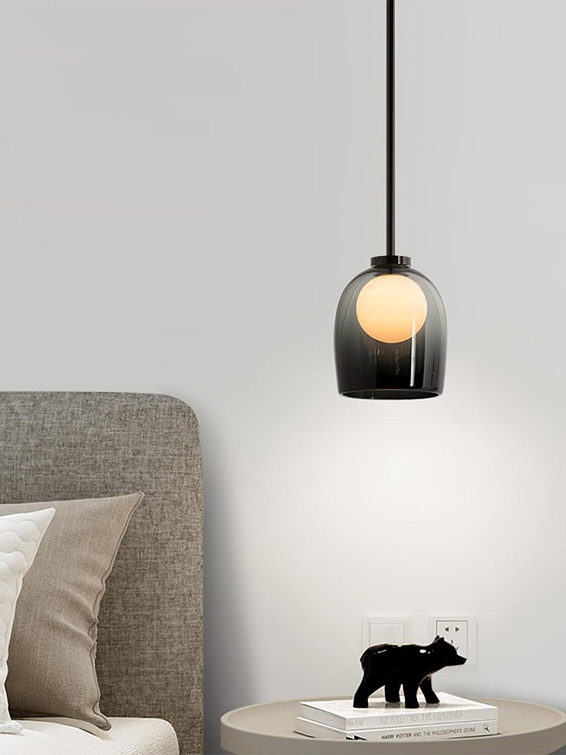 Illuminated gradient-black Crux pendant above a bedside table beside an upholstered bed