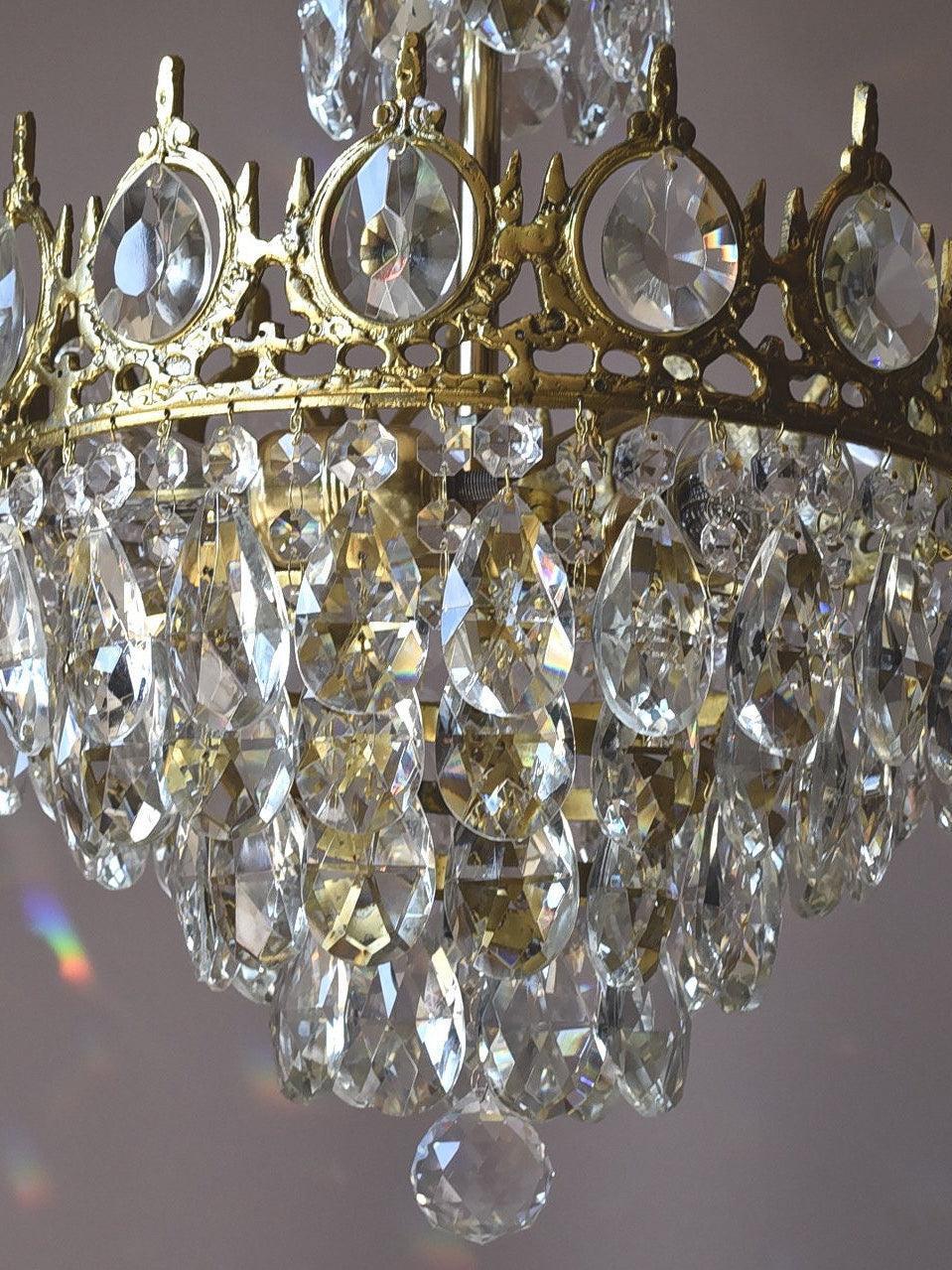 Detail of an ornate crown ring with round faceted inserts above rows of clear hanging crystal drops