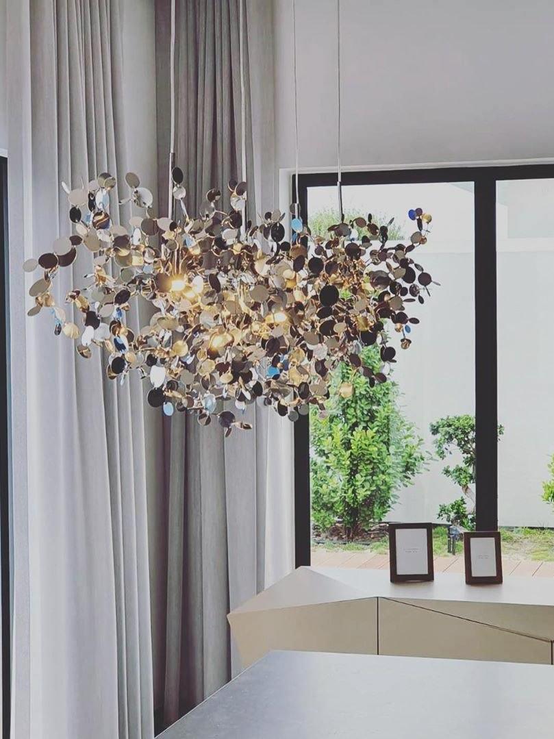 Warm gold-toned metal-disc chandelier beside a tall curtained window