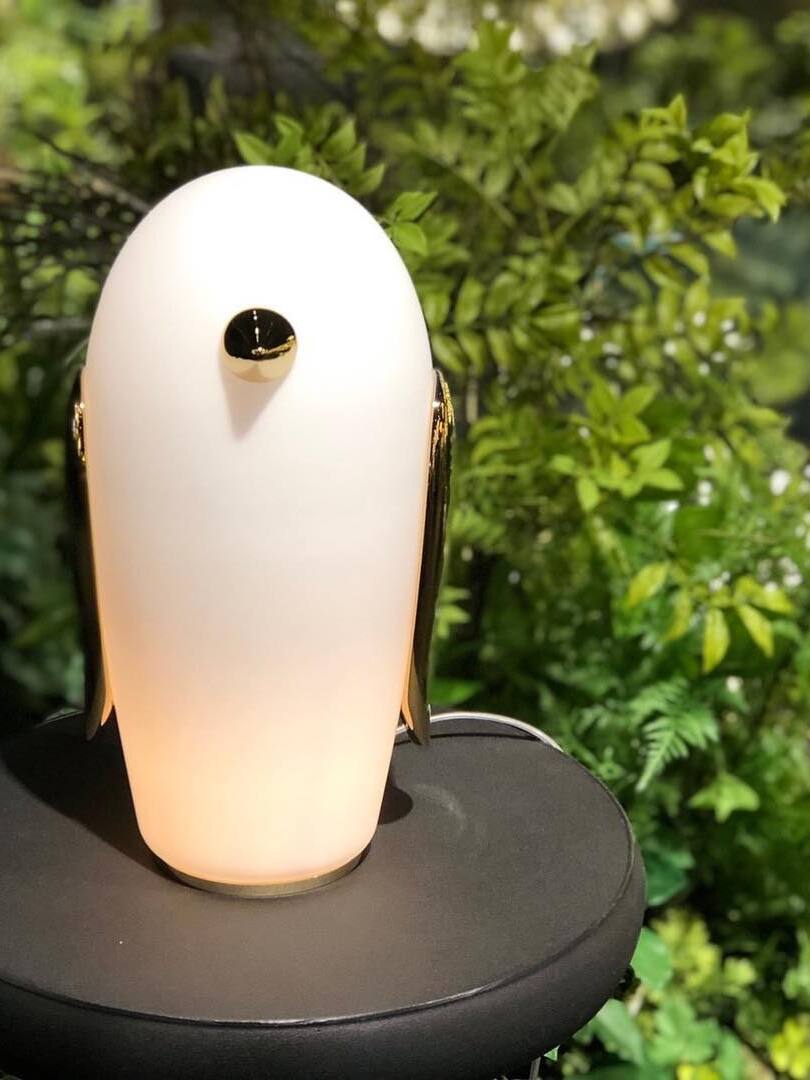 Closer lit white penguin on black round table before green foliage
