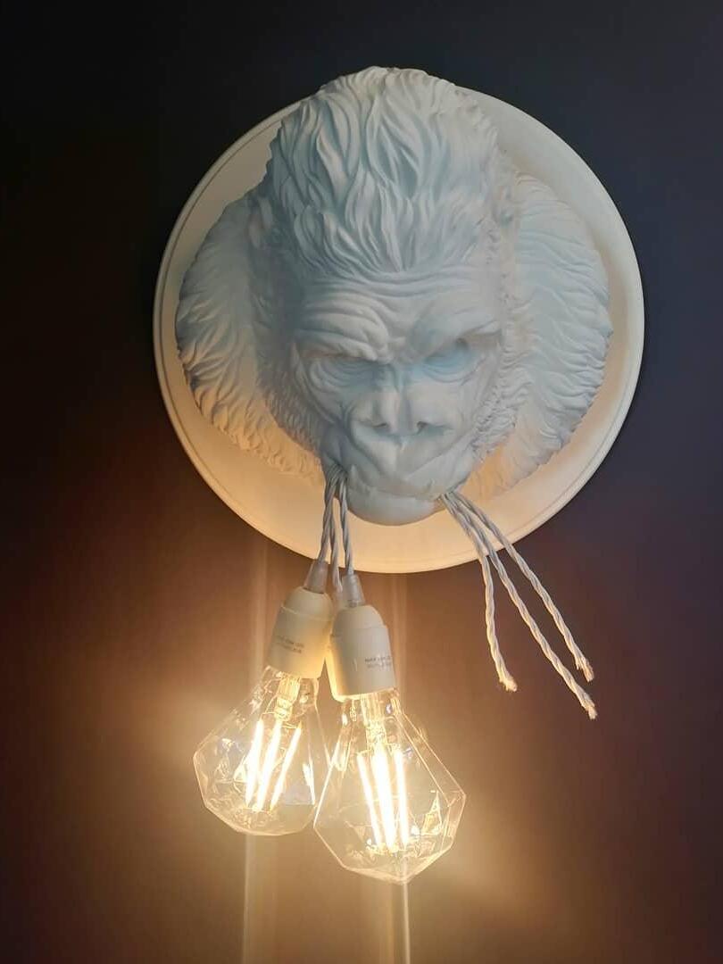 White gorilla face with glowing diamond-shaped bulbs in warm-lit dark view