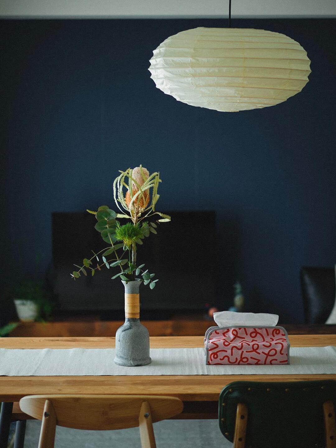 Pale paper lantern over a wooden dining table with flower arrangement and patterned tissue box against a blue wall
