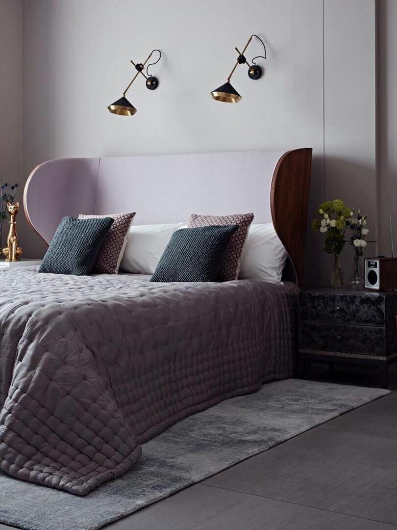 Two black cone wall lights with crossing arms above a gray winged headboard and patterned cushions