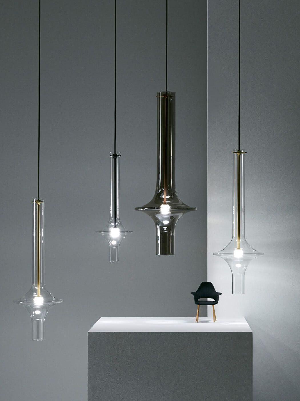 Four clear and smoky flared glass pendants at staggered heights around a white display block with a miniature black chair