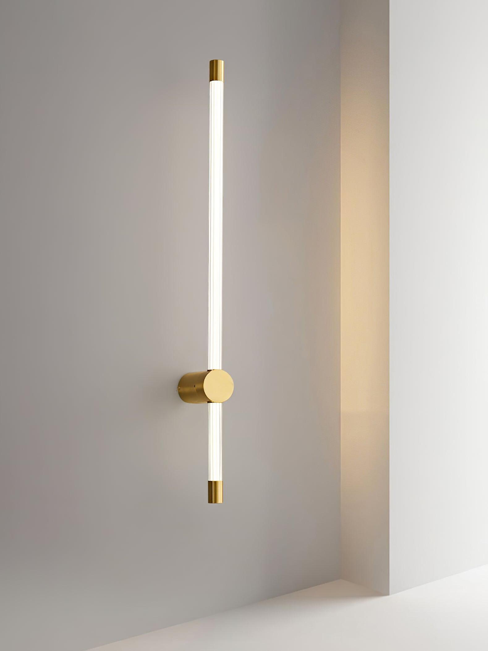 Brass-tone long-and-short tube wall light mounted vertically beside a window ledge