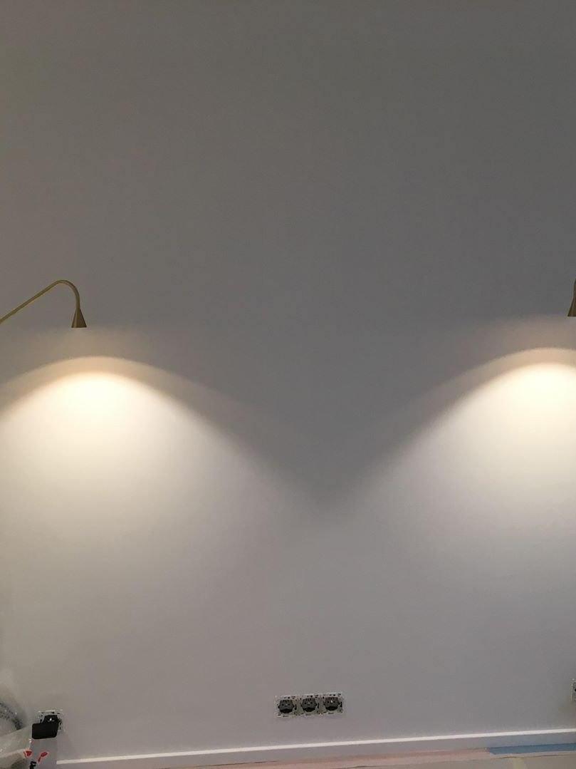 Small wall-light heads casting light above bedside positions