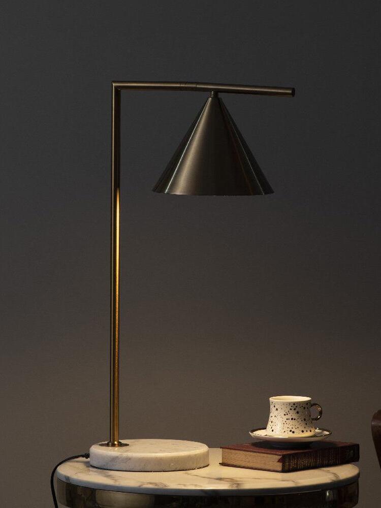 Dimly lit cone lamp beside cup and books on marble table