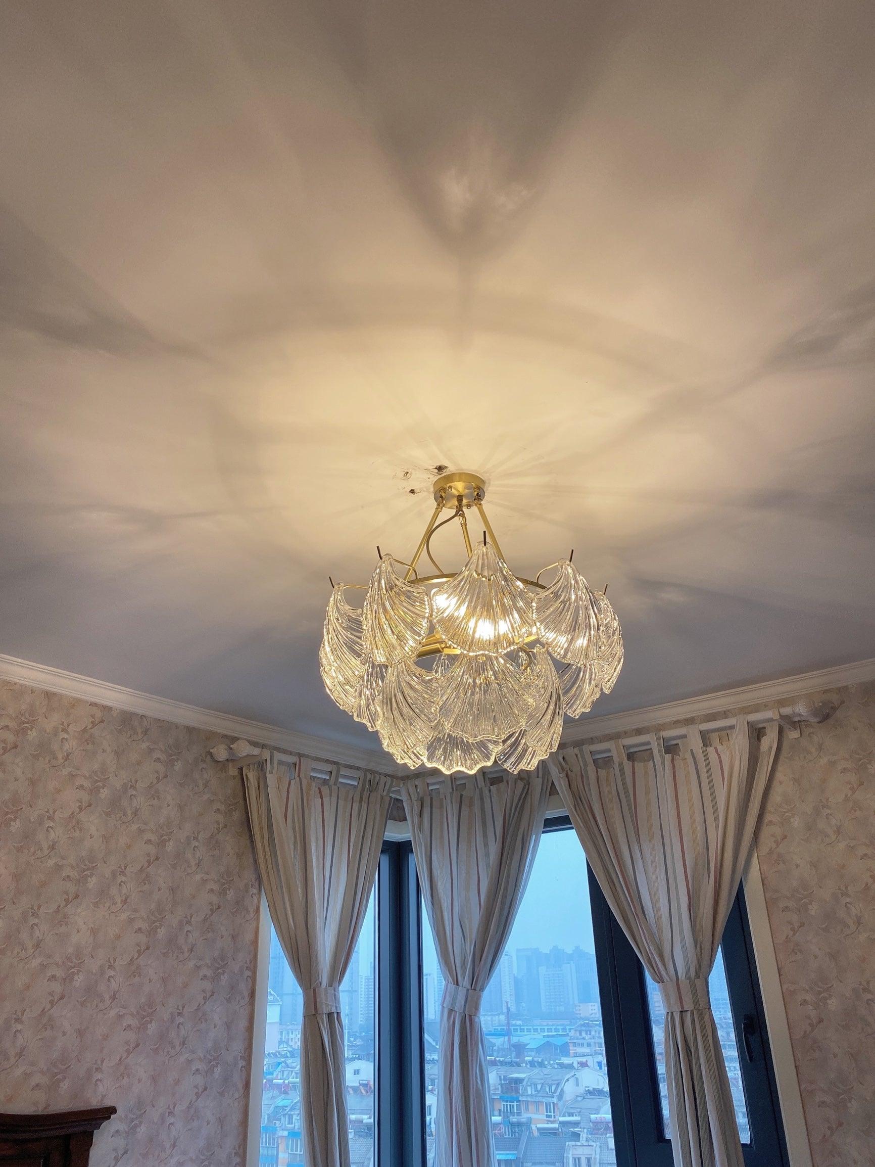 Low-angle view of illuminated shell panels with warm-looking ceiling patterns near window curtains