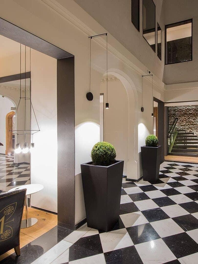 Black cable pendants along a tall hall with planters and a checkerboard floor