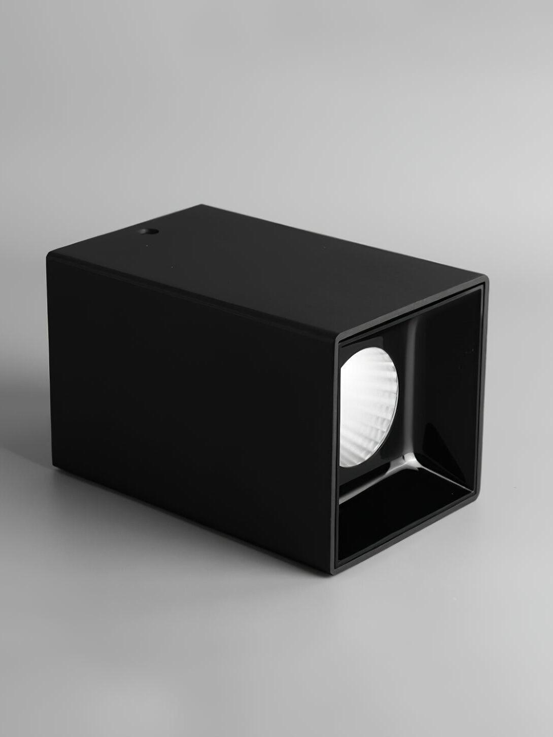 Black metal spotlight lying on its side, with a round reflector inside a glossy black square recess