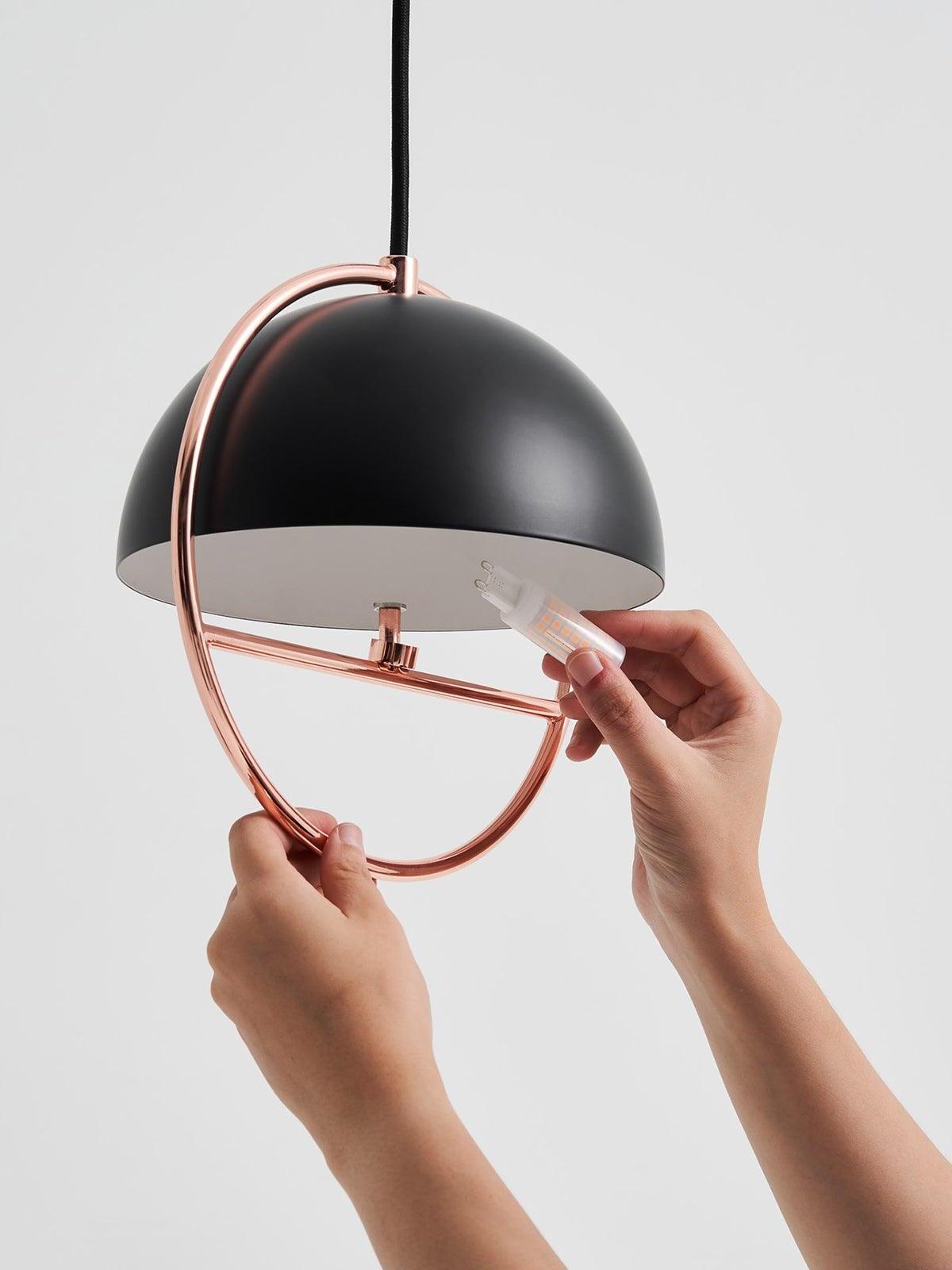 Hand holding small bulb beneath black ring pendant