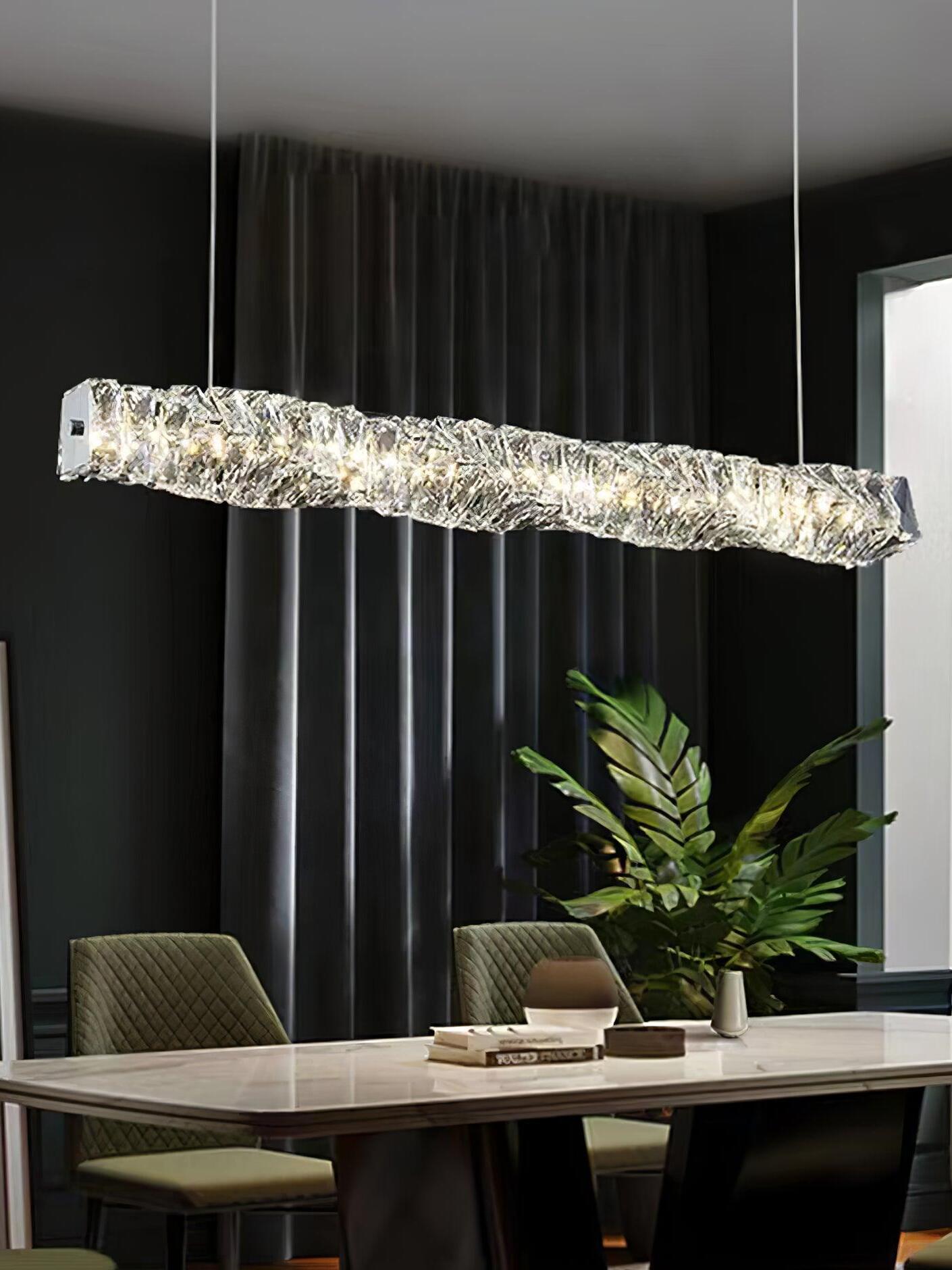 Linear crystal pendant above a table with green chairs beside dark curtains and a leafy plant