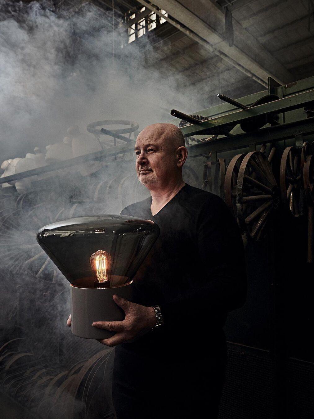 Person holding lit smoky glass lamp with cylindrical base in workshop