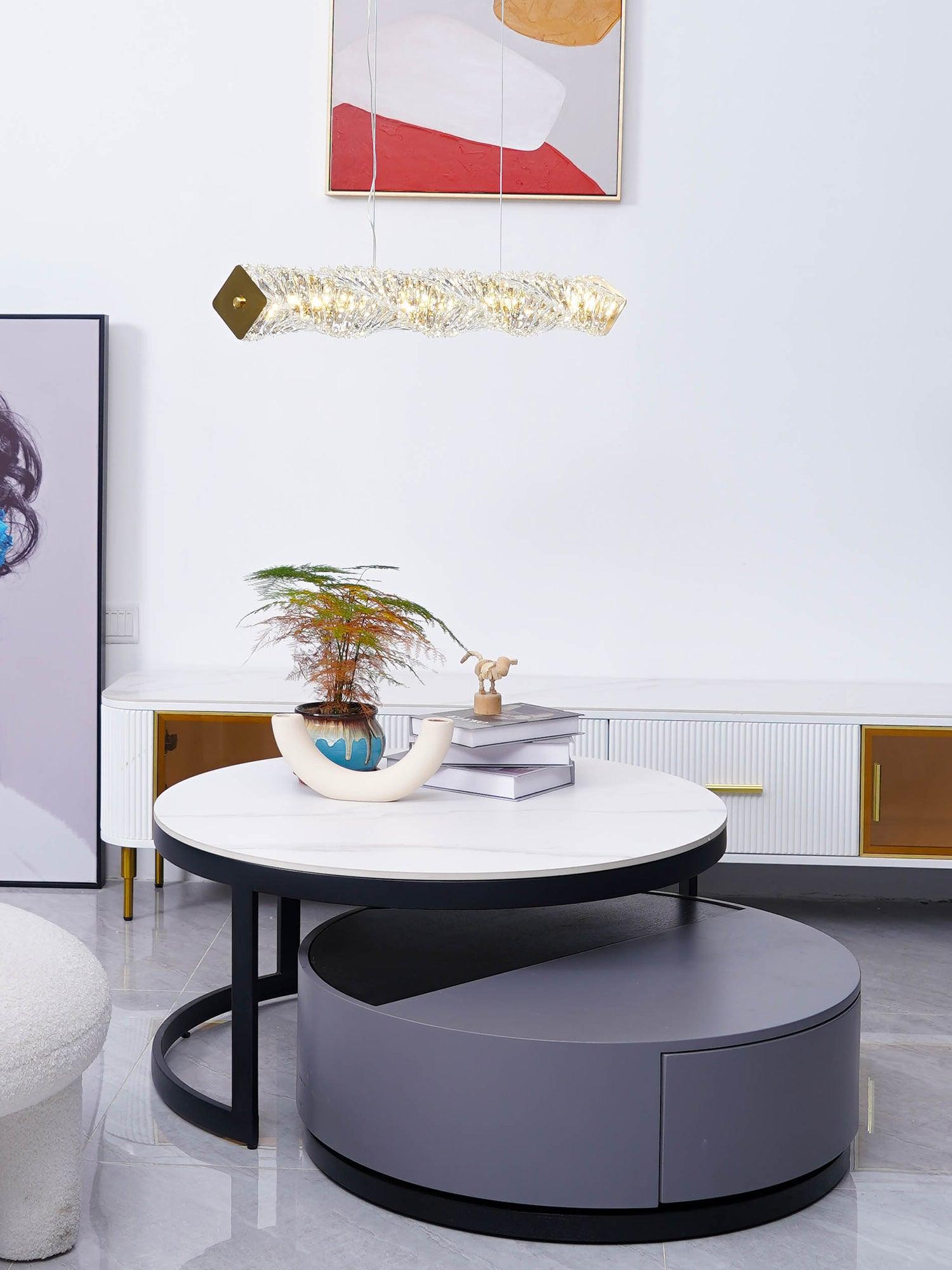 Long crystal pendant in a living room above stacked round coffee tables with books and a plant