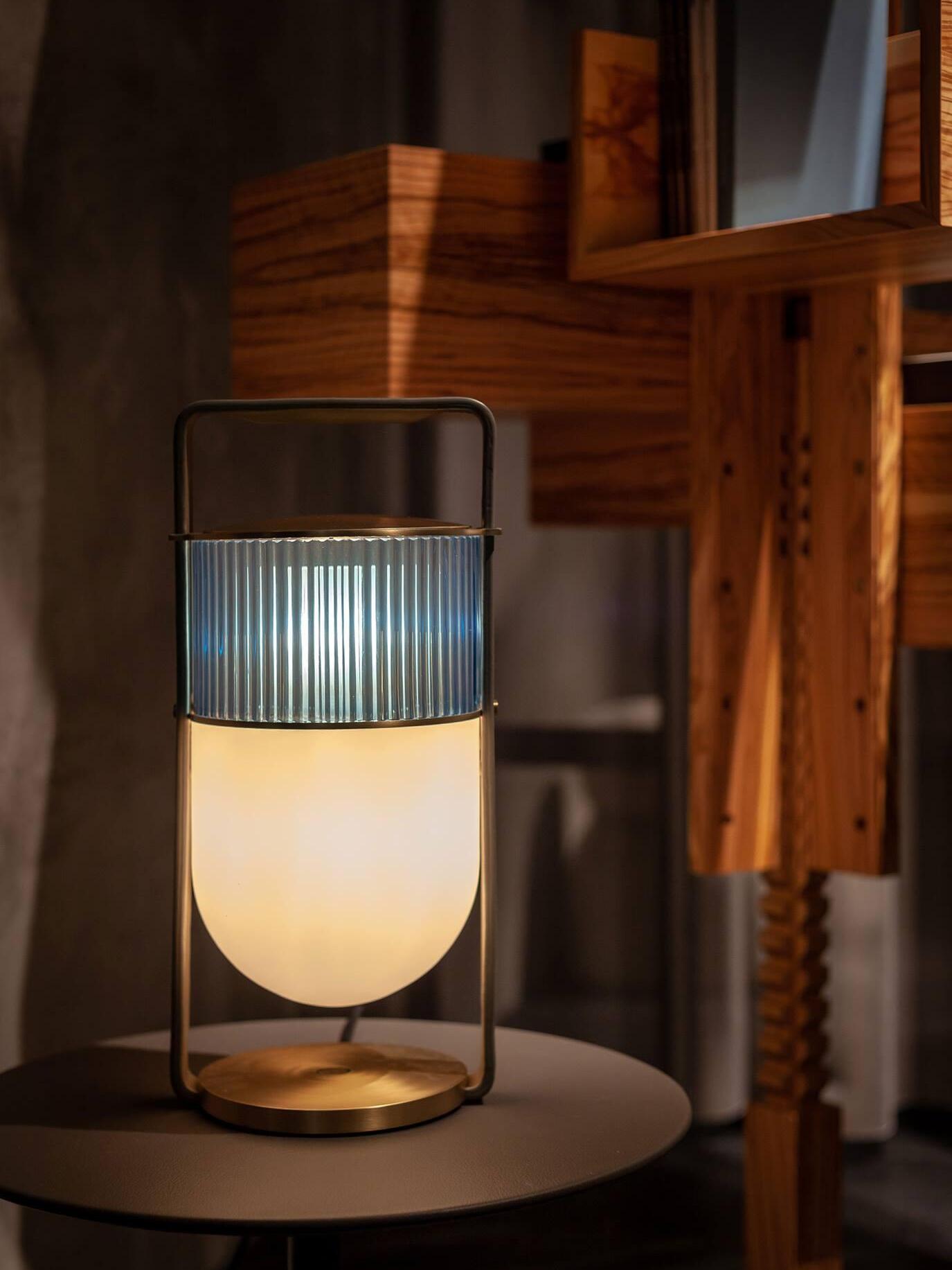 Xi lamp glowing against dark wood, showing ribbed upper glass, rounded lower shade and gold-tone base