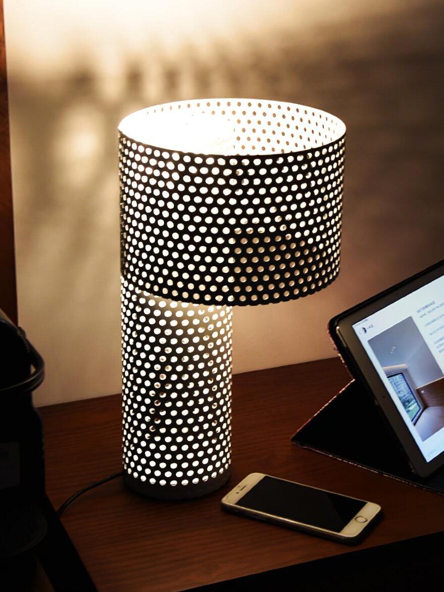 Lit perforated table lamp beside tablet and phone