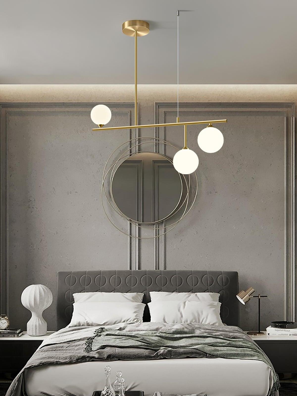 Three-globe Arteriors chandelier above a bed with a padded headboard and round wall mirror