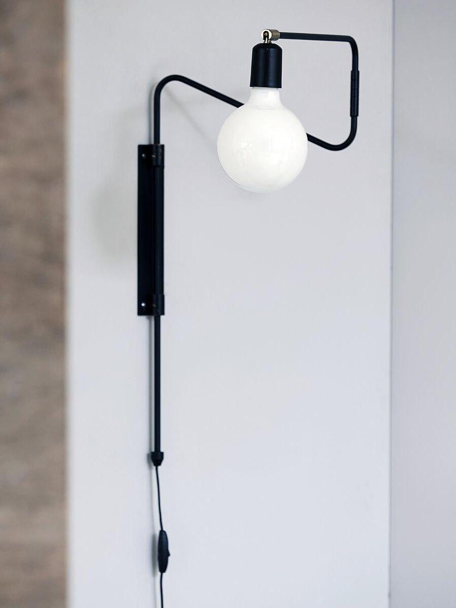 Black wall lamp with folded bent arm, exposed white globe bulb and cord-mounted inline switch
