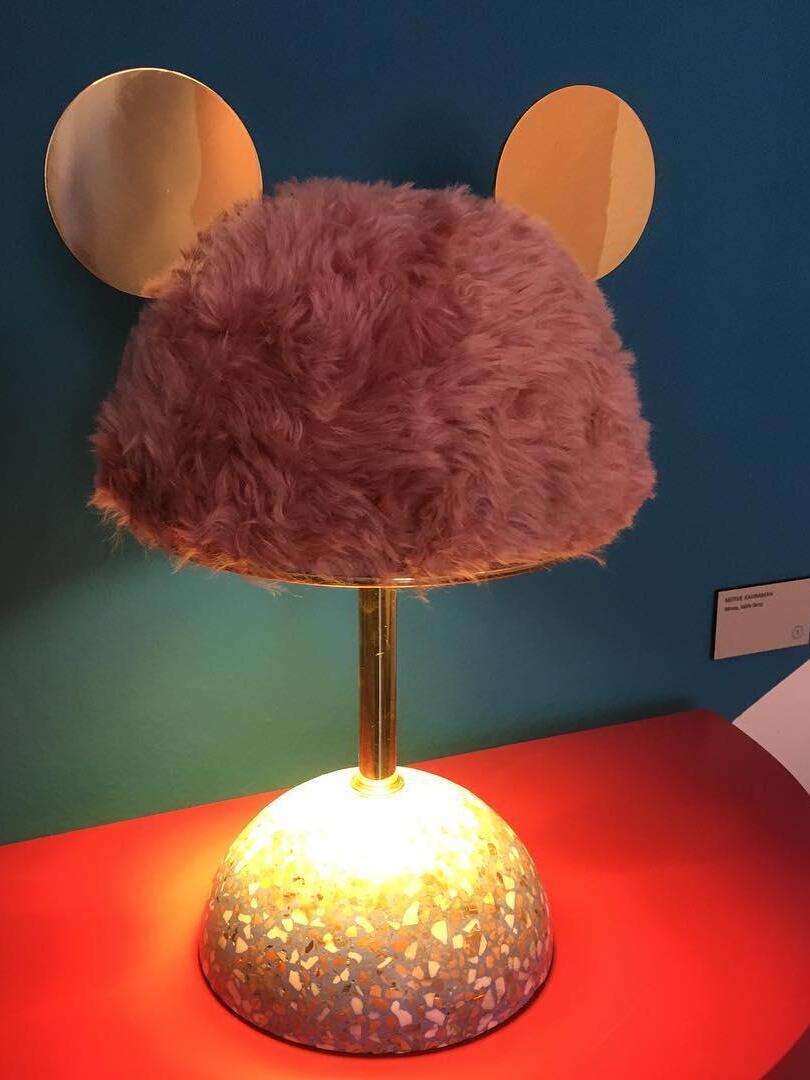 Pink plush shade lamp with bright light around speckled base on red exhibition surface