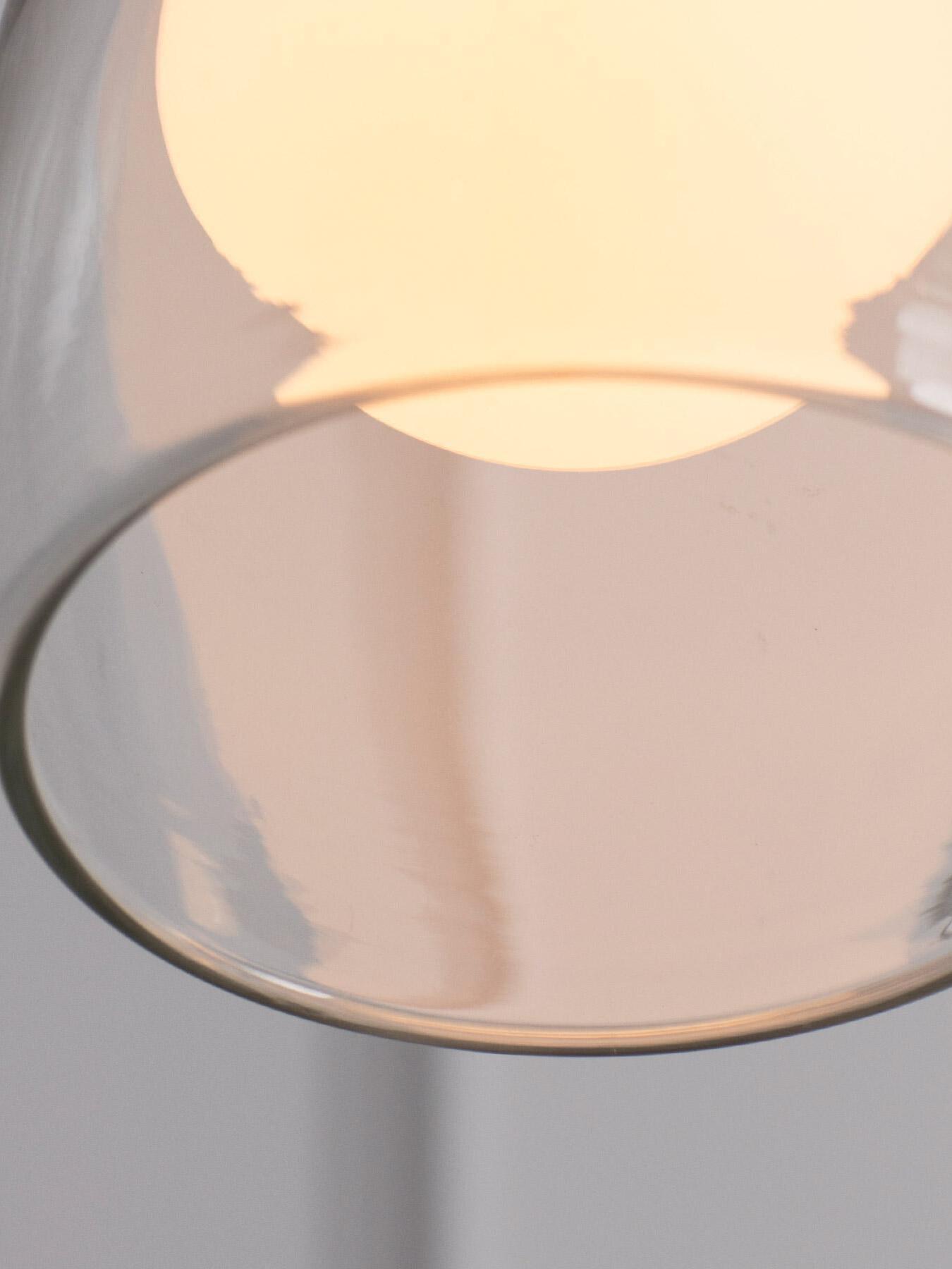 Close-up of the open lower rim of a clear Crux glass shade beneath its glowing sphere