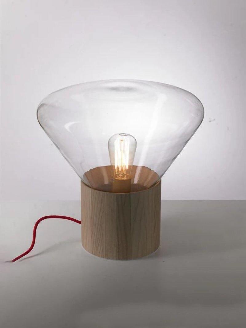Clear glass lamp with darker wood base and red cord trailing left