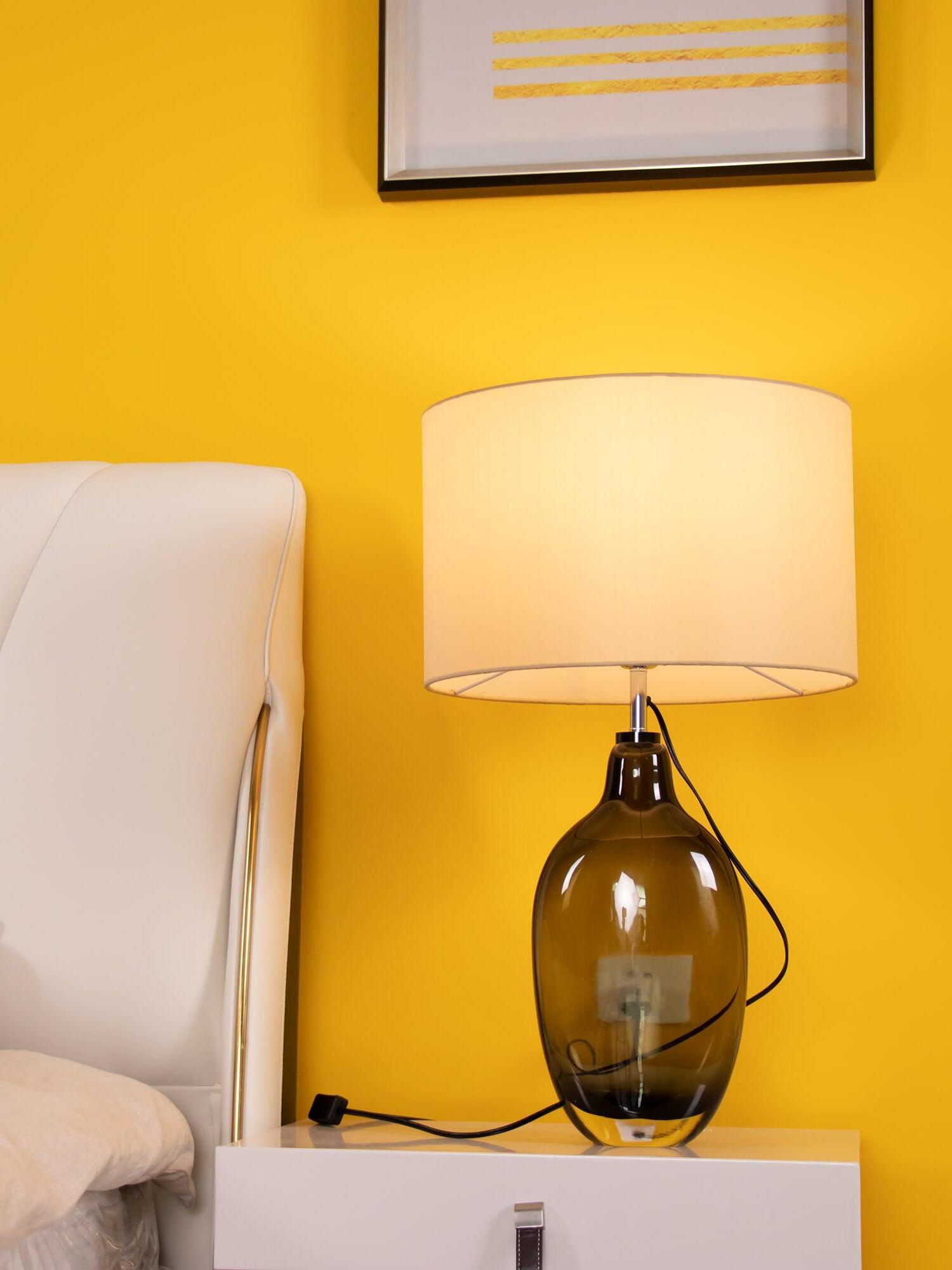 Lit table lamp against yellow wall with visible inline cord switch