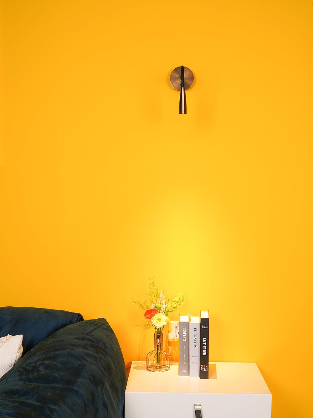 Bronze-toned Flexi nearly straight down on a yellow wall, with flowers and books on a cabinet below