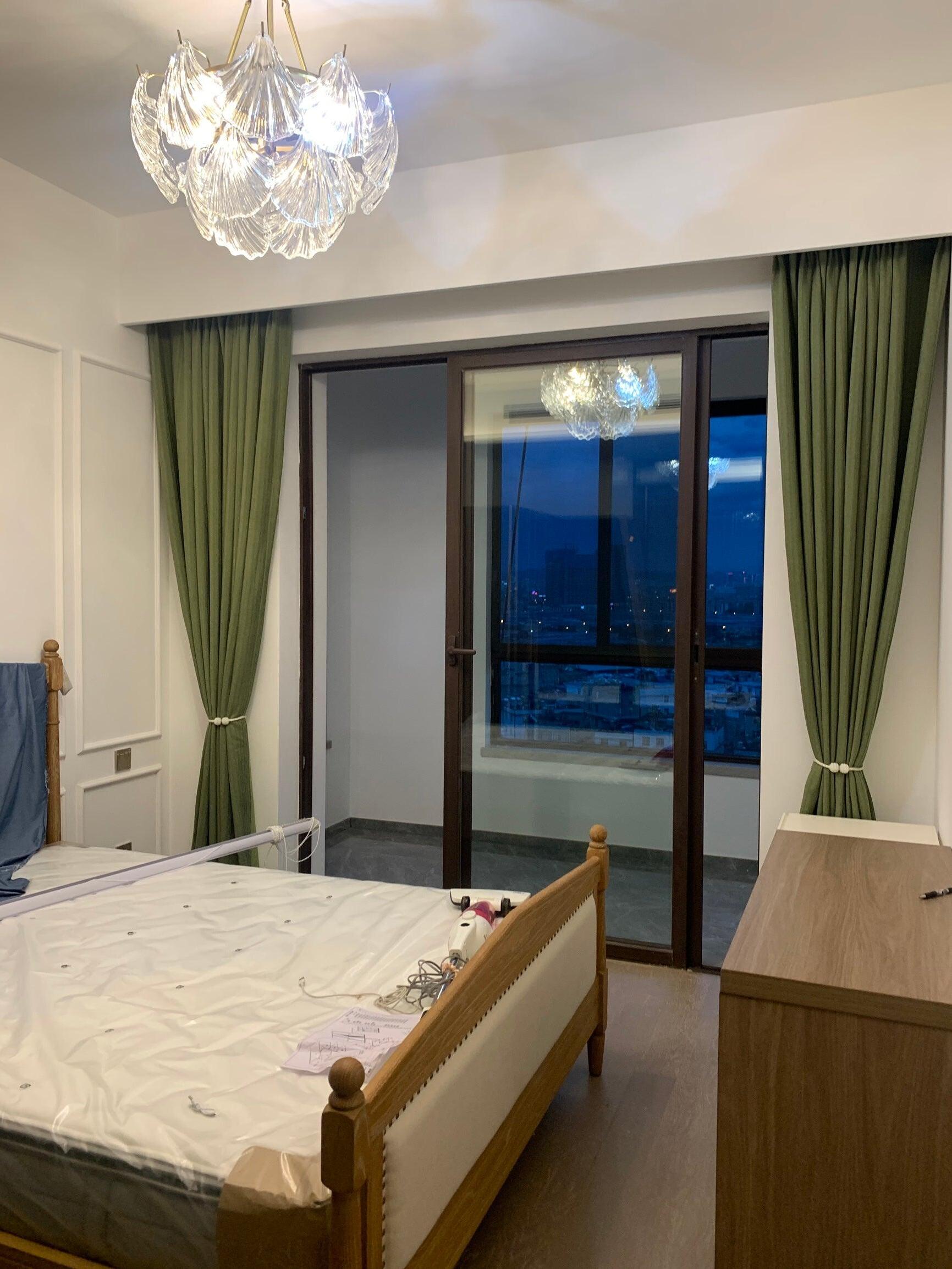 Glass ceiling light above a wooden bed near green curtains and a glass door