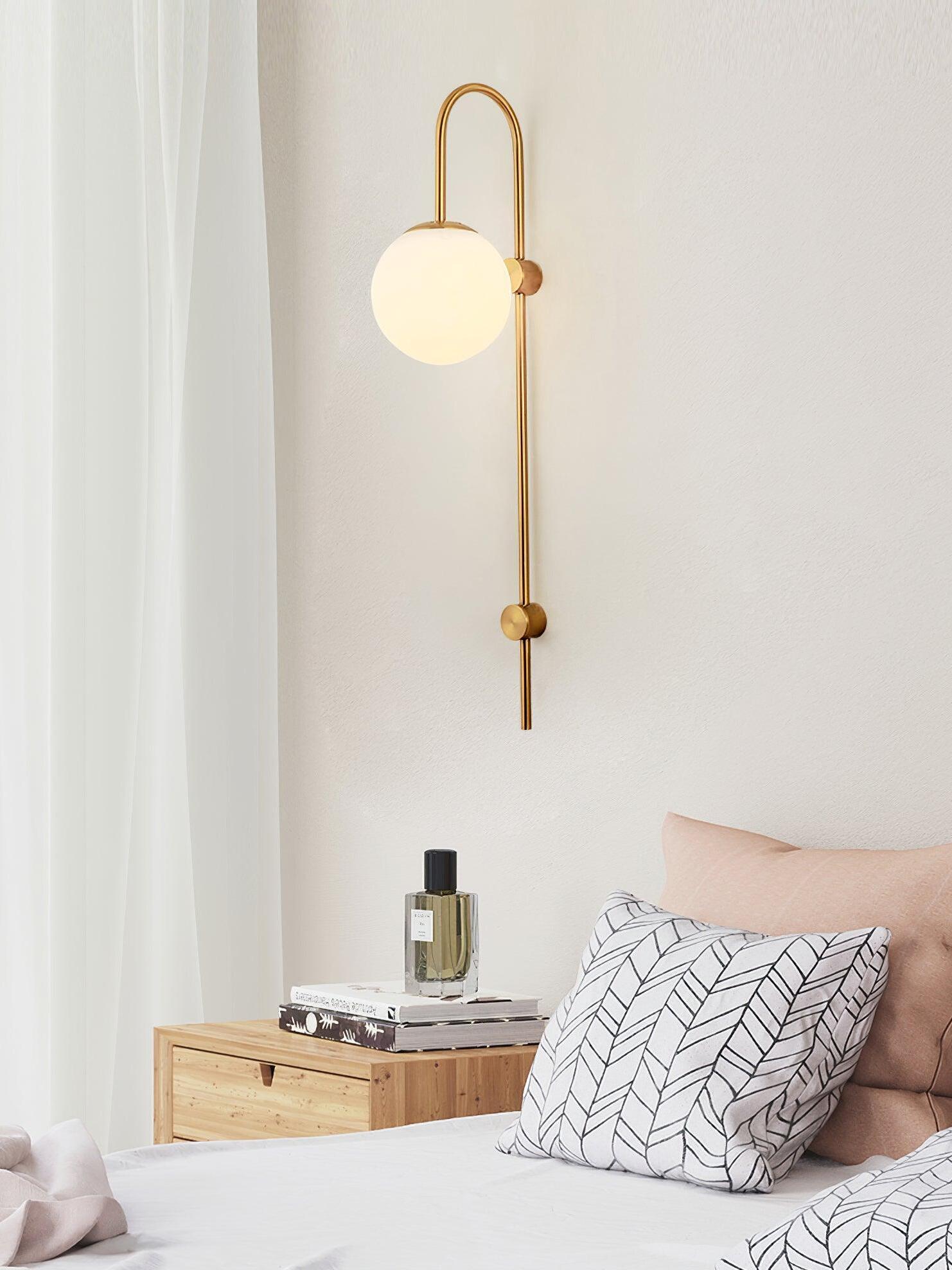 Gold globe wall sconce beside bed and pale curtains