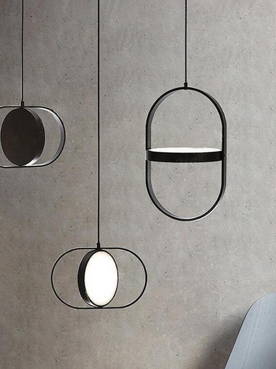 Three black oval-frame disc pendants, with glowing faces and an edge-on disc, against a concrete wall