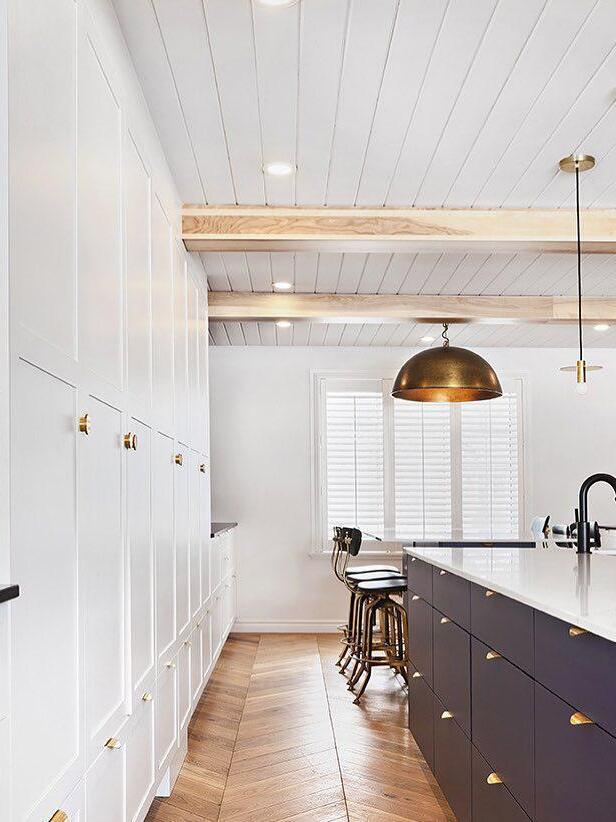 Brass-tone disc pendant in a white kitchen with ceiling beams and a separate large dome-shade light