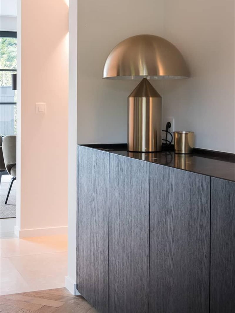 Gold-tone mushroom lamp with a visible cord on a dark counter above gray cabinetry