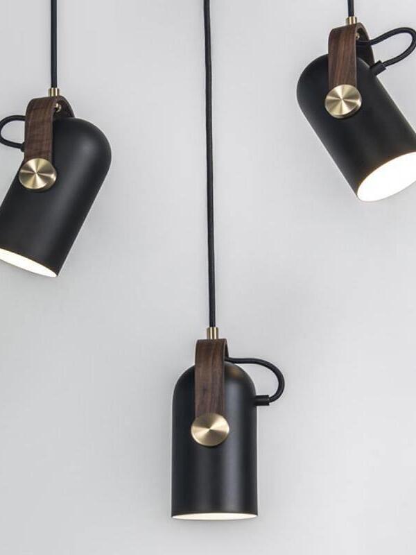 Three lit black cylindrical pendant heads at varied angles and heights, with wood brackets and gold-tone pivots