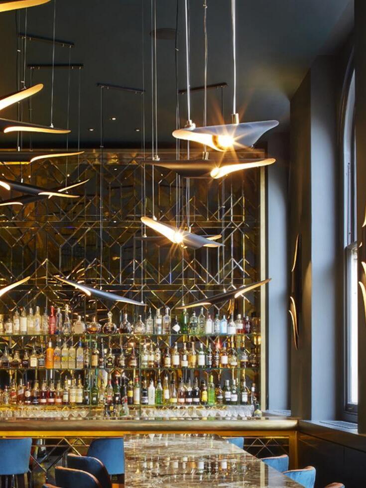 Separate pipe pendants above a bar with bottle shelves, mirrored wall and blue chairs