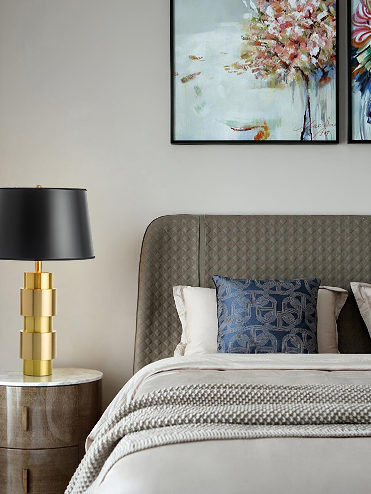 Jean lamp beside a bed with a blue patterned cushion and floral wall art