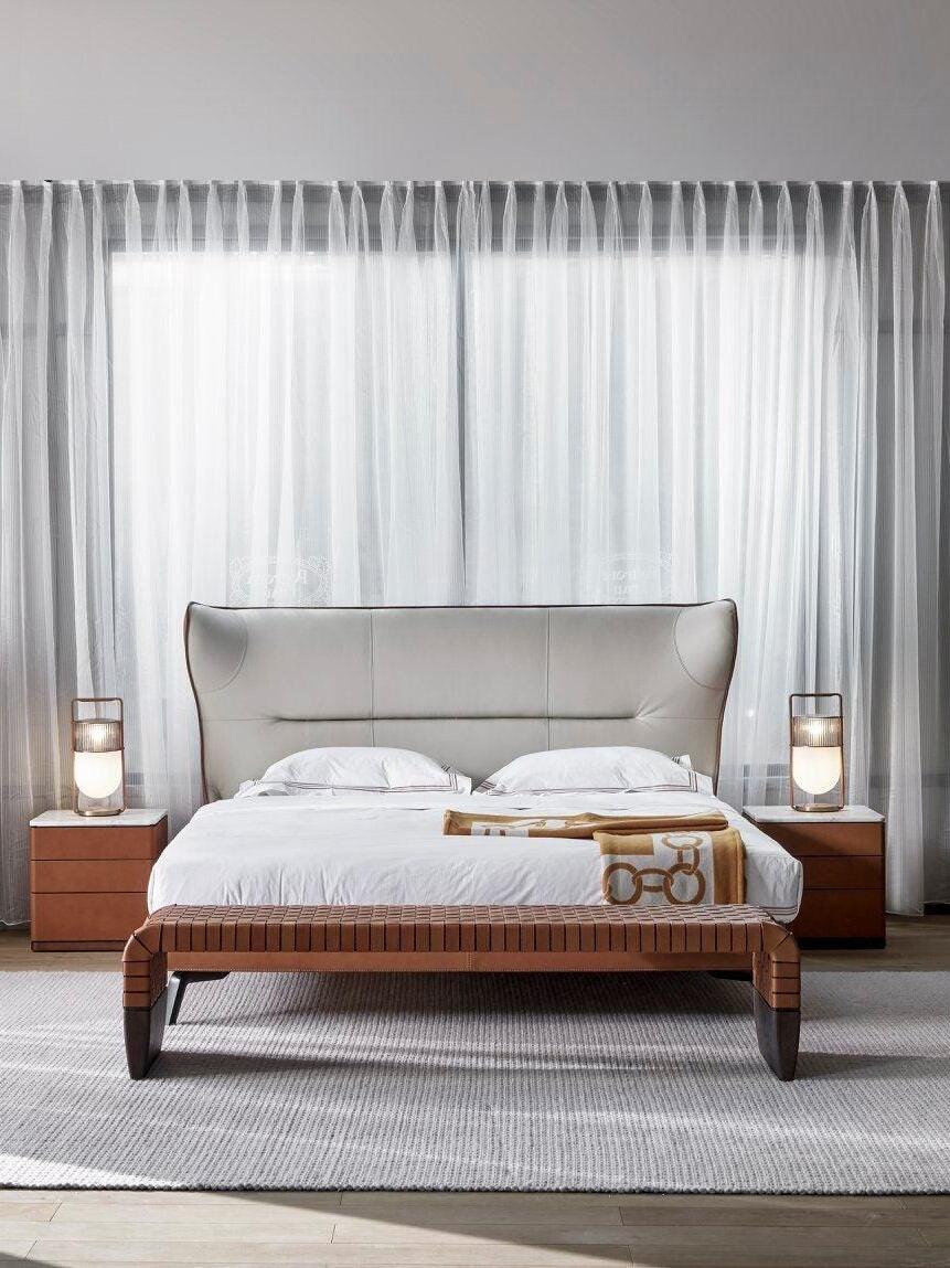 Front view of a bedroom with lamps on both bedside tables, full-height curtains, a rug and bench