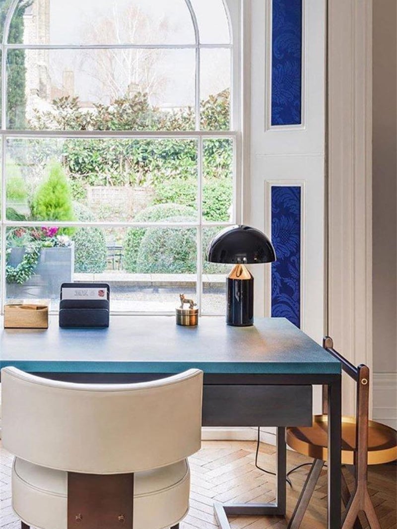 Glossy black mushroom lamp with a gold-tone cone area on a blue desk beside a large window