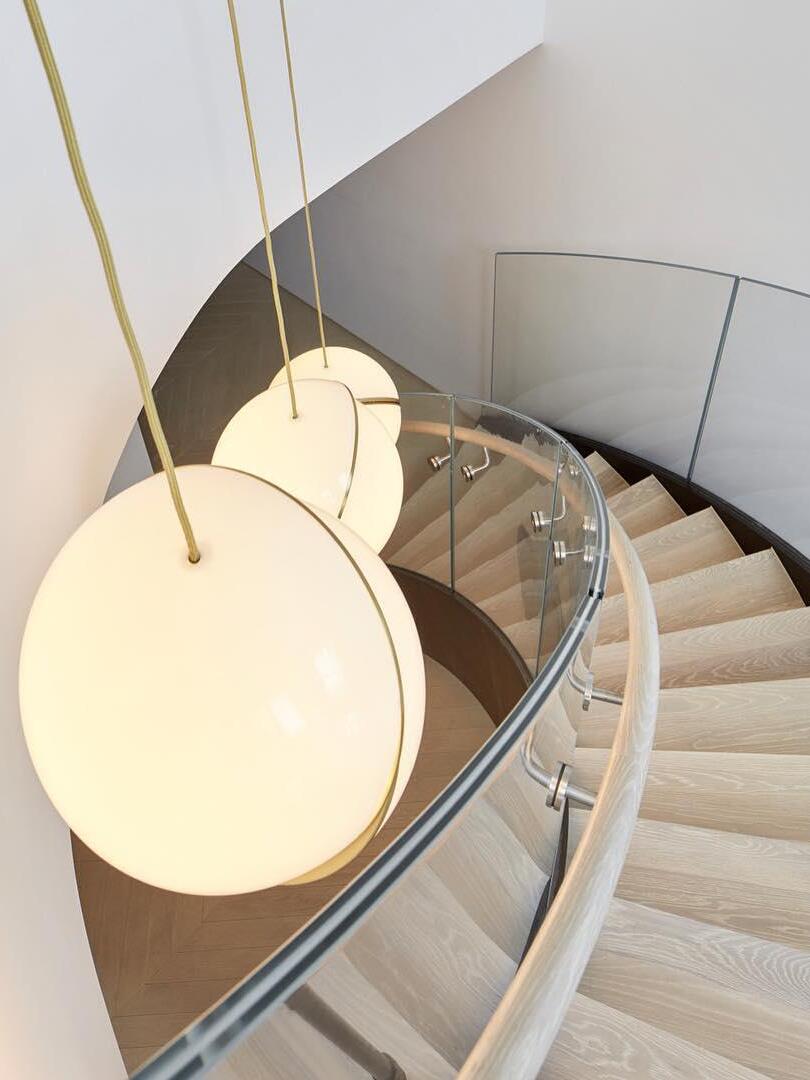 Three illuminated Crescent globe pendants beside curved wooden stairs and a glass balustrade